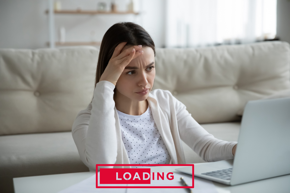 A frustrated woman sitting on a floor looking at a laptop with a red "LOADING" bar overlay, illustrating slow computer performance before an SSD upgrade.